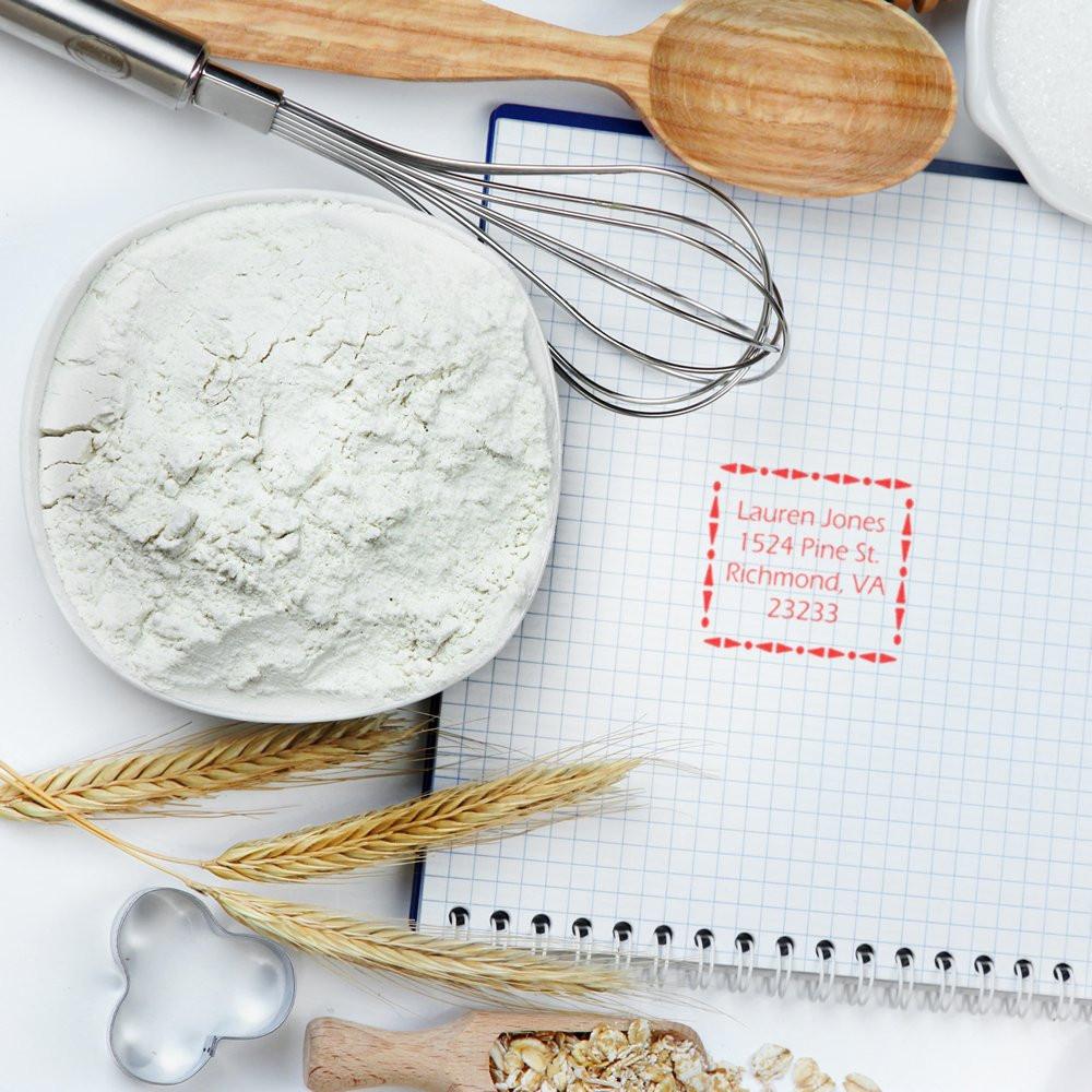 Custom address rubber stamp on recipe notebook with baking tools and ingredients for personalized branding.