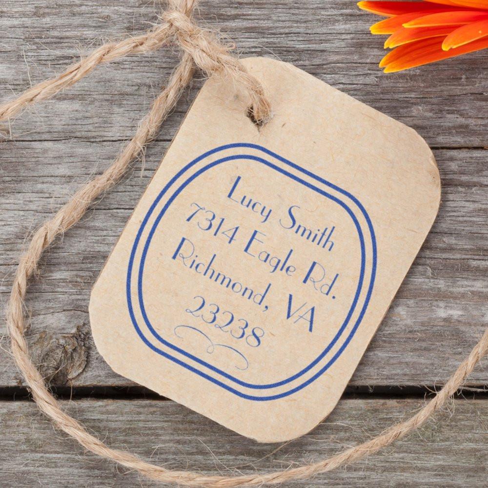 Custom return address rubber stamp on kraft paper tag with blue ink, displayed on rustic wood with twine