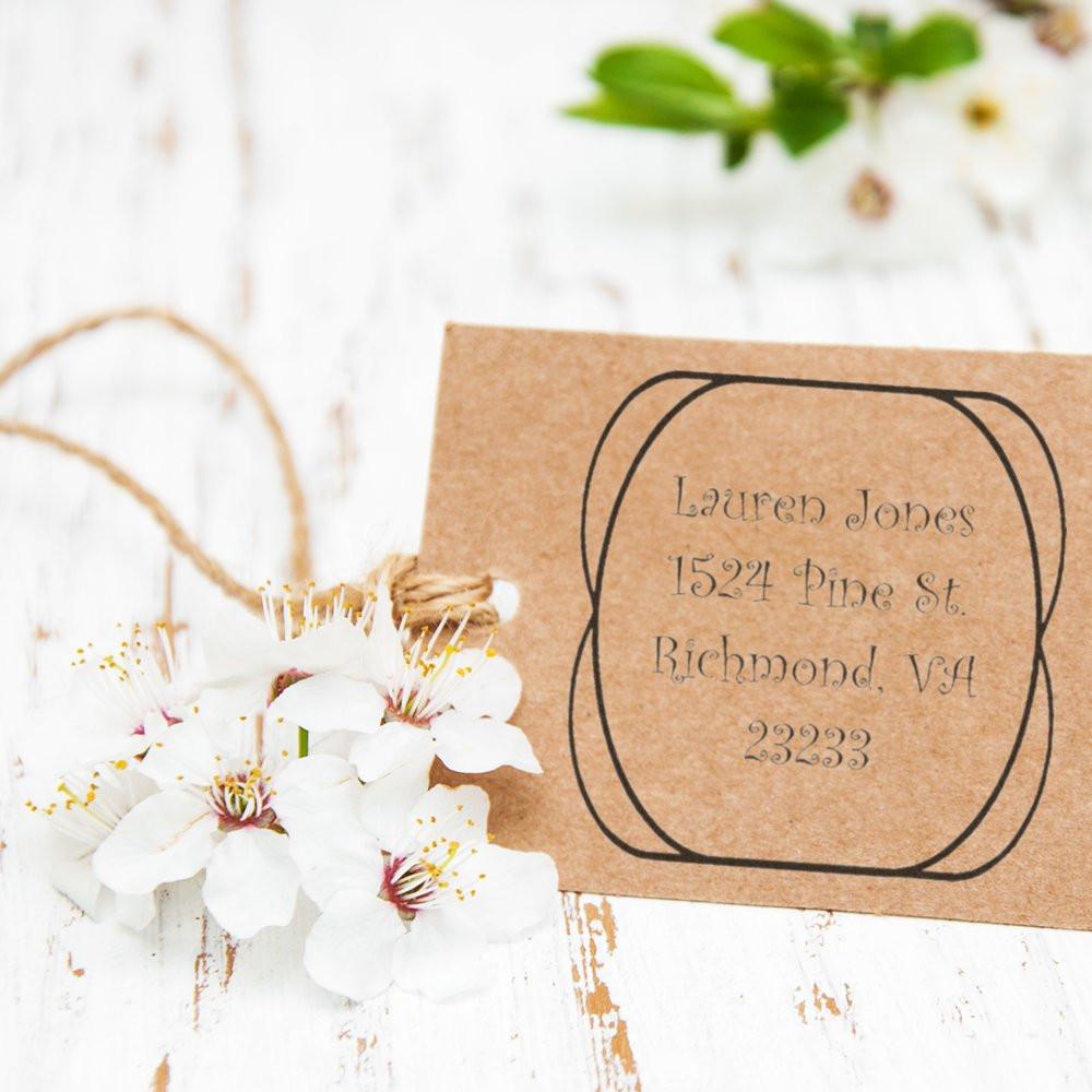 Custom return address rubber stamp on kraft paper with white flowers for personalized wedding stationery.