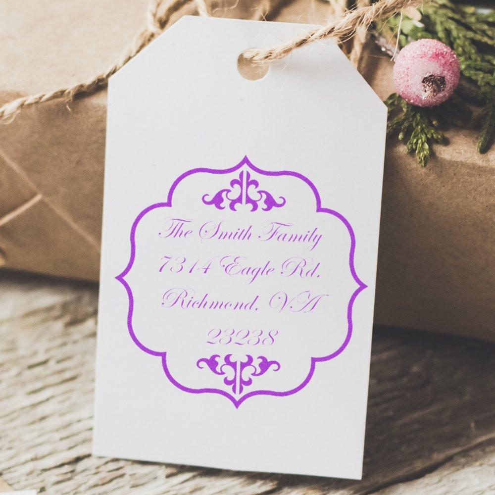 Personalized return address rubber stamp on a gift tag with elegant purple monogram design for custom mailing and packaging.