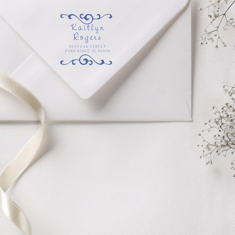 Custom return address rubber stamp on a wedding envelope with blue floral design and Kaitlyn Rogers name and address.
