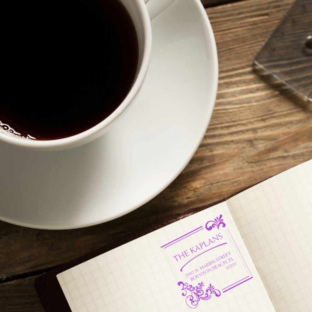 Custom purple return address rubber stamp for The Kaplans on a notebook beside coffee, ideal for personal stationery.