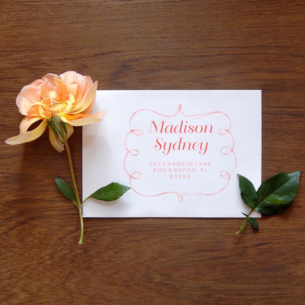 Floral wedding invitation card on wooden table reading Madison Sydney with address, featuring a peach rose and green leaves.