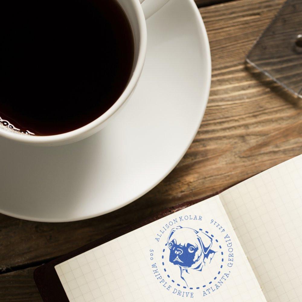 Custom pet address rubber stamp impression on notebook beside coffee cup, featuring a dog portrait and circular return address.