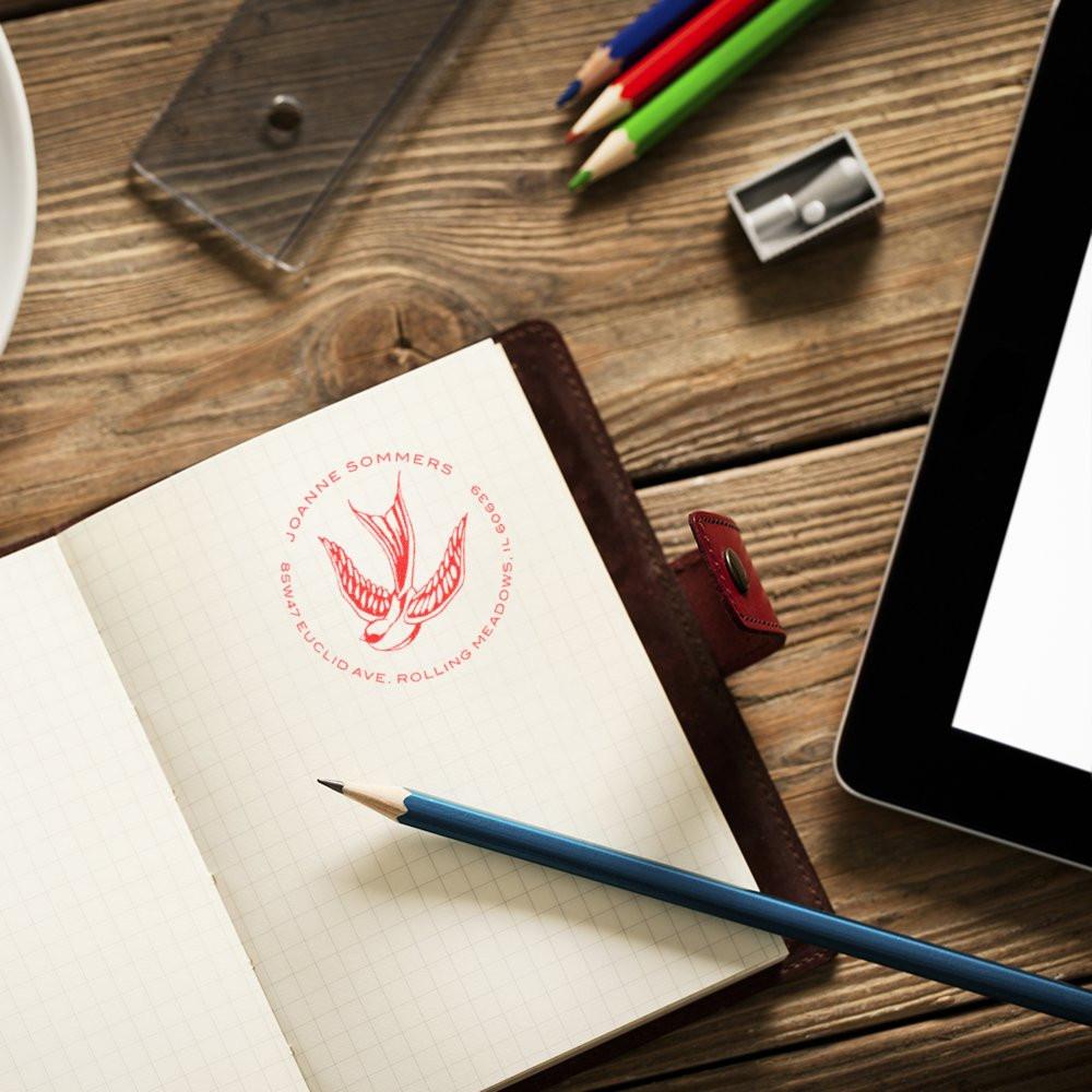Custom address rubber stamp with bird logo on notebook, ideal for personalized mailing and branding.