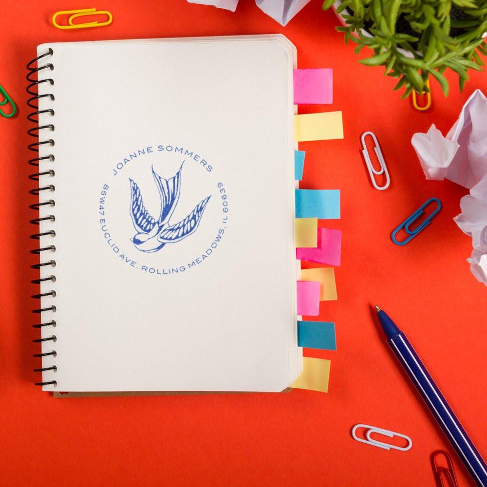 Custom return address rubber stamp on notebook, featuring bird logo for stationery, branding and wedding invitations.