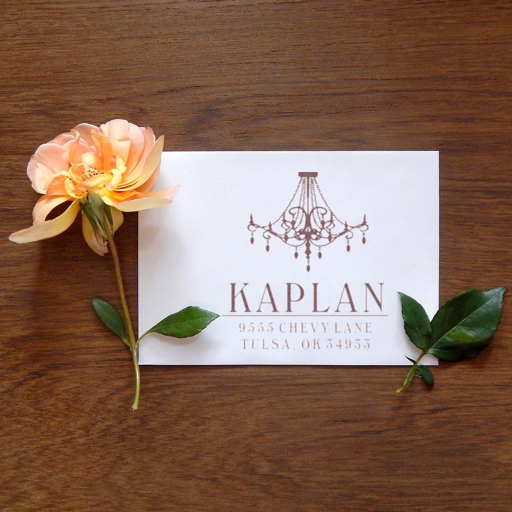 Kaplan Chevylane business card with chandelier logo, framed by peach rose on wooden table.