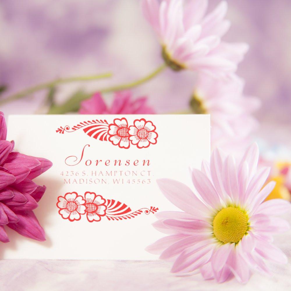 Personalized floral return address rubber stamp with red flower accents, shown on a white card surrounded by pink daisies.