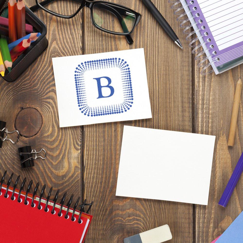 Custom rubber stamp design mockup with blue letter B on a desk, alongside blank card and stationery for branding.