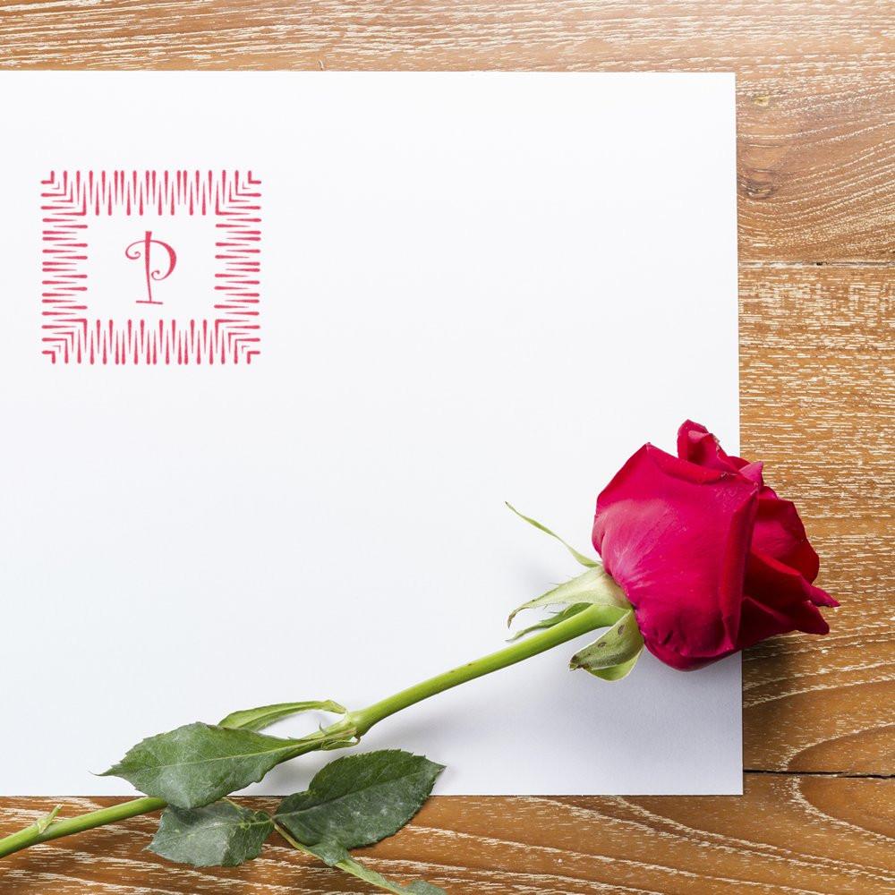 Red rose beside white Valentine greeting card with pink monogram P on wooden table, romantic message backdrop gift for love today.