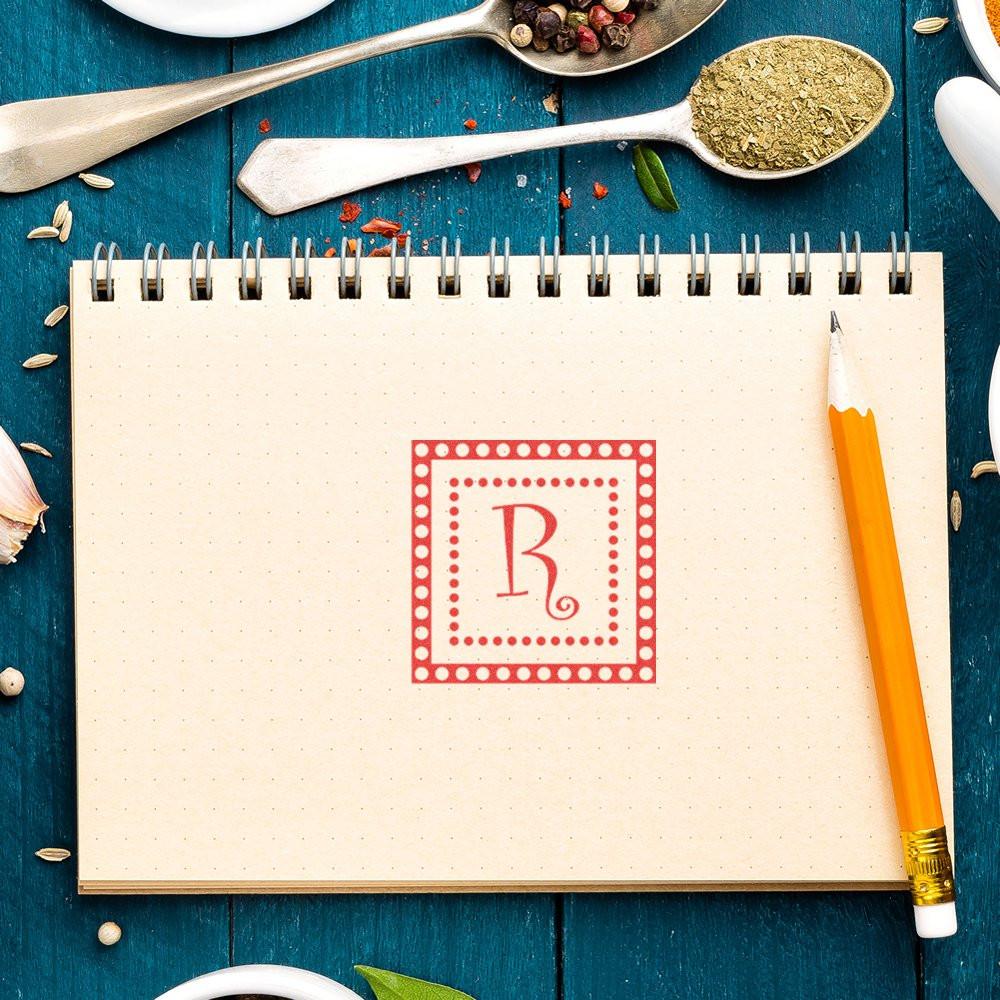 Red monogram rubber stamp impression on notebook page for personalized stationery, branding, and craft projects.