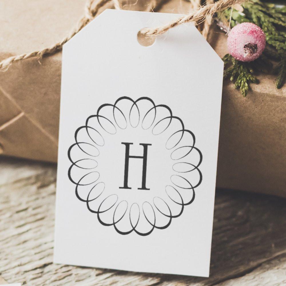 Personalized holiday gift tag with letter H in ornate frame, on rustic craft background with Christmas ornaments and twine decoration.