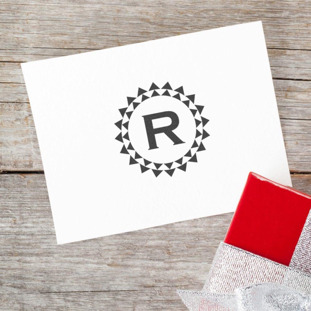 Custom rubber stamp logo with letter R on card, beside red stamp tool on wood background for branding and packaging.
