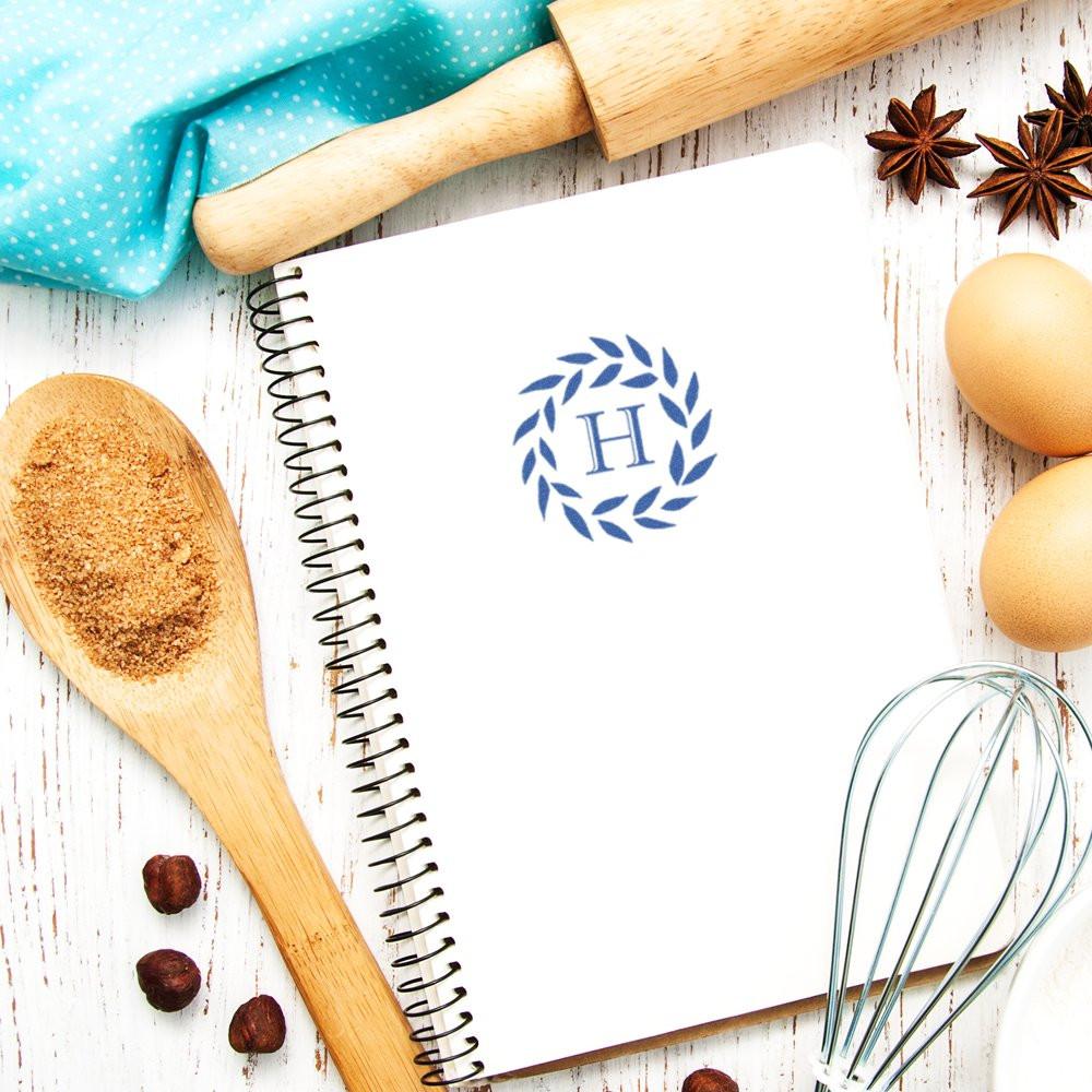 Custom monogram rubber stamp on recipe notebook, styled in a baking flat lay with rolling pin, whisk, eggs, and spices.