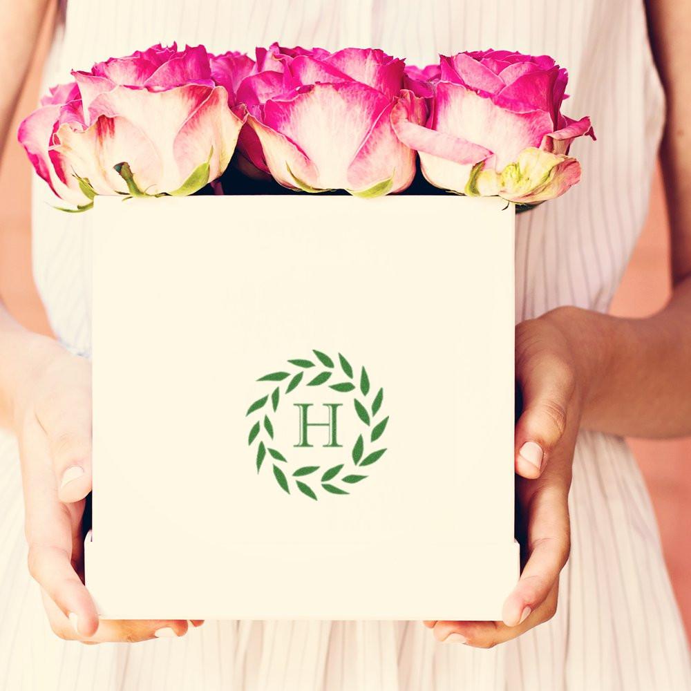 Custom monogram rubber stamp with laurel wreath logo on a floral gift box for elegant wedding or packaging branding
