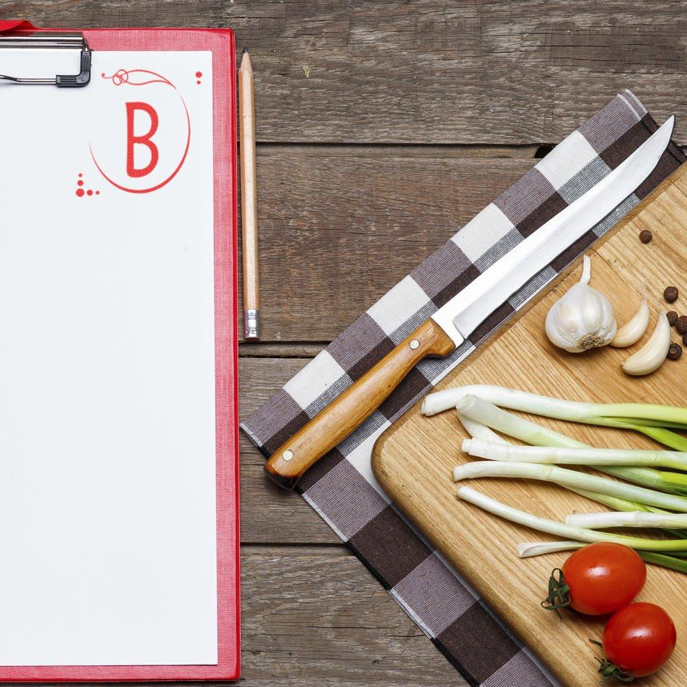 Custom rubber stamp letter B on recipe clipboard with kitchen ingredients, perfect for branding food prep and organization.