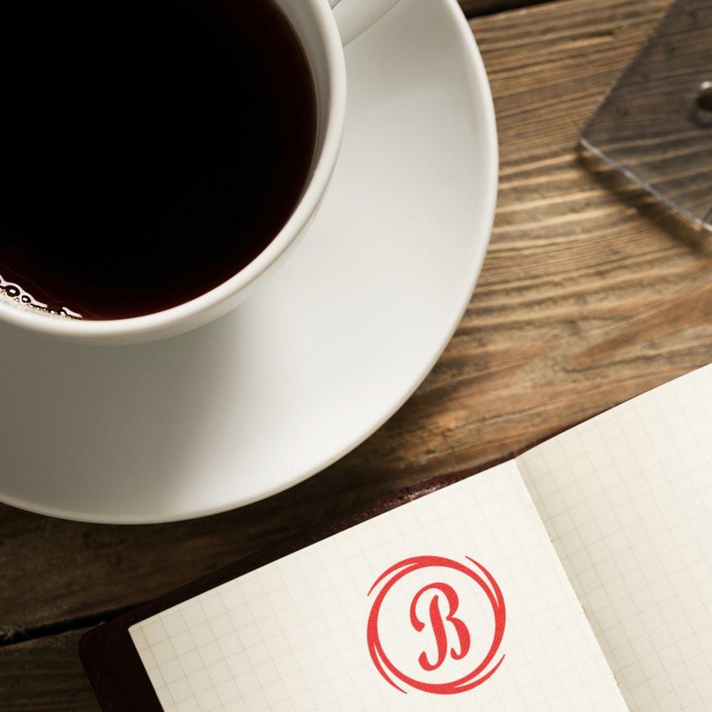 Personalized monogram rubber stamp with red letter B on notebook beside coffee cup on a rustic wooden desk
