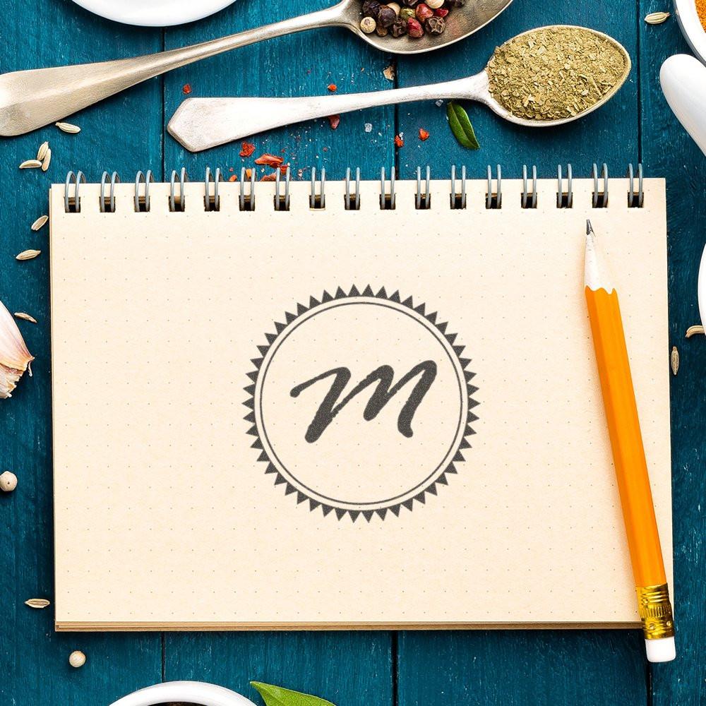 Custom monogram rubber stamp with letter M on a notebook, perfect for personalized branding, crafts, and stationery.