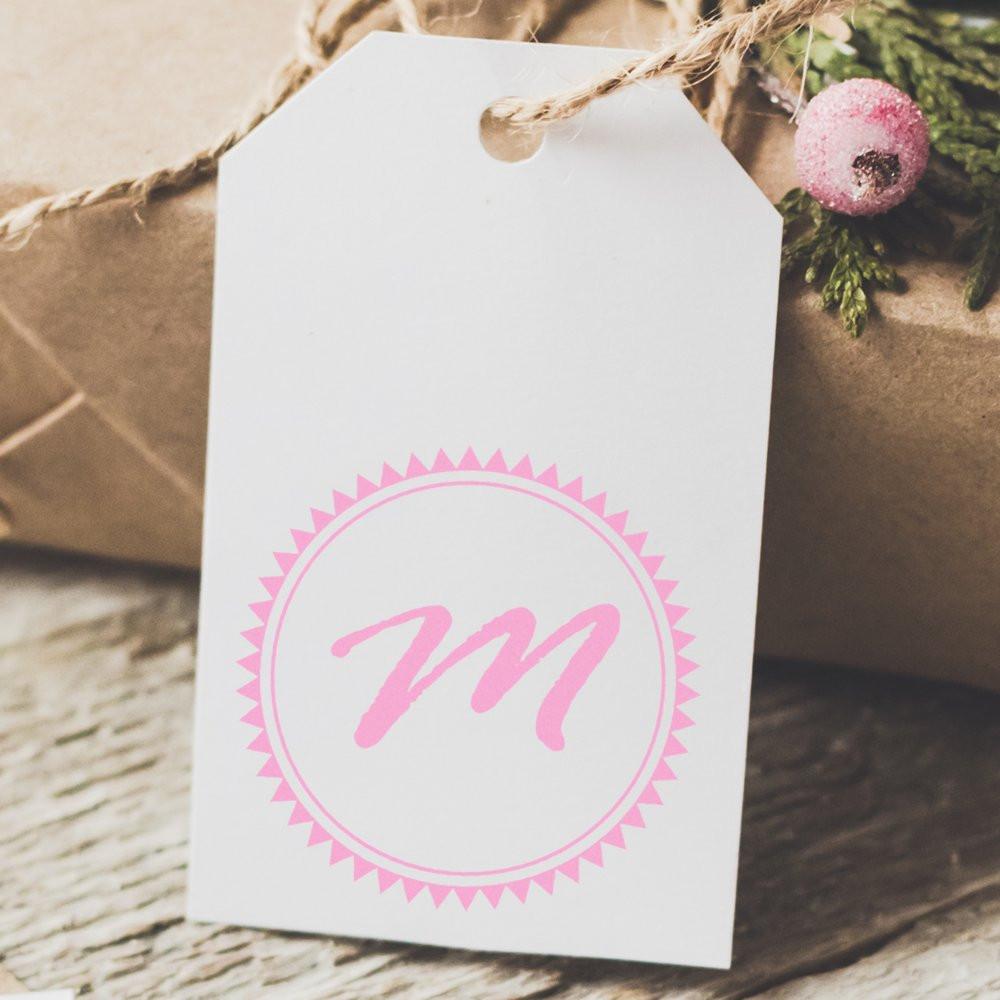 Custom pink monogram rubber stamp design on a white gift tag for personalized holiday packaging.