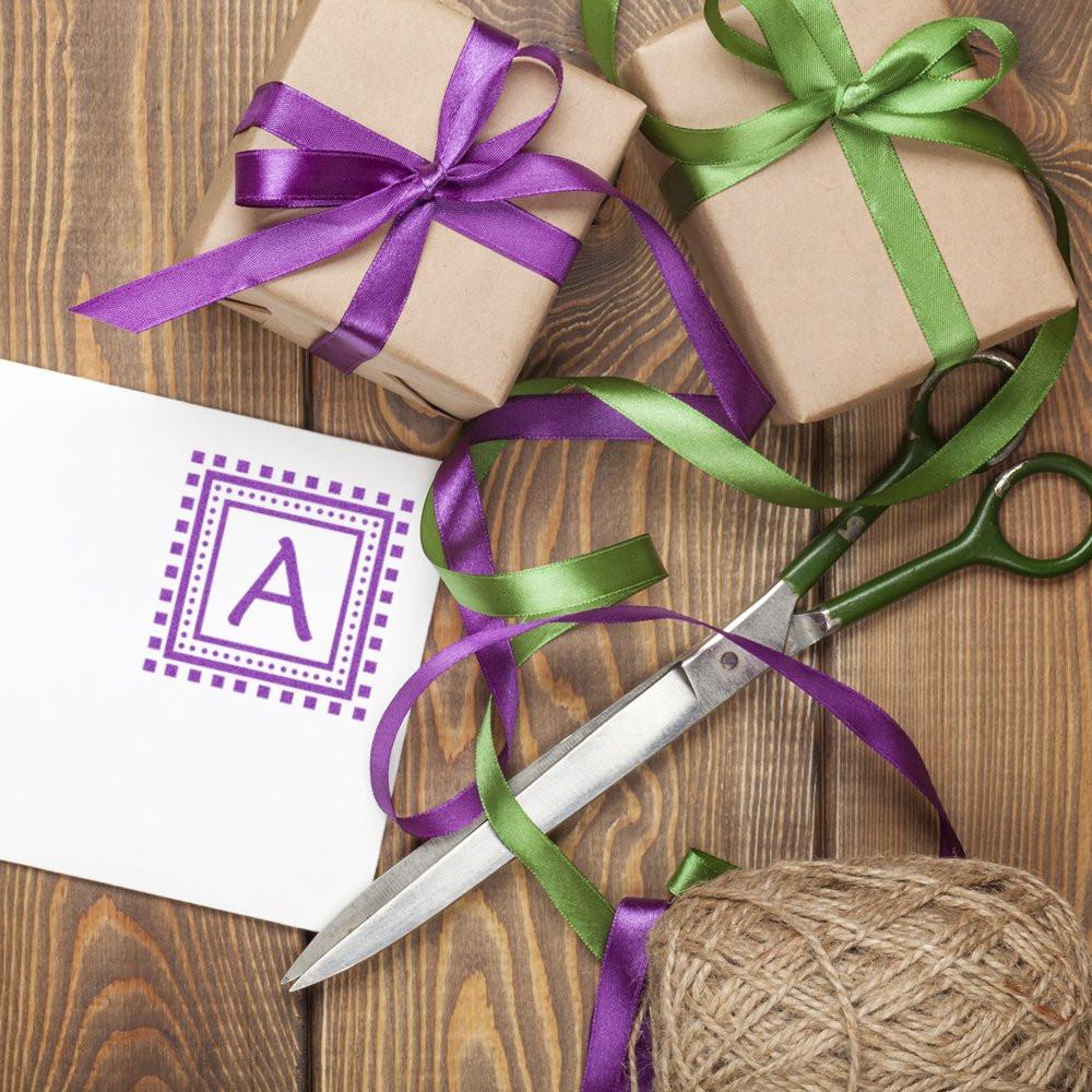 Purple letter A rubber stamp on gift wrapping with ribbon and scissors for personalized packaging.