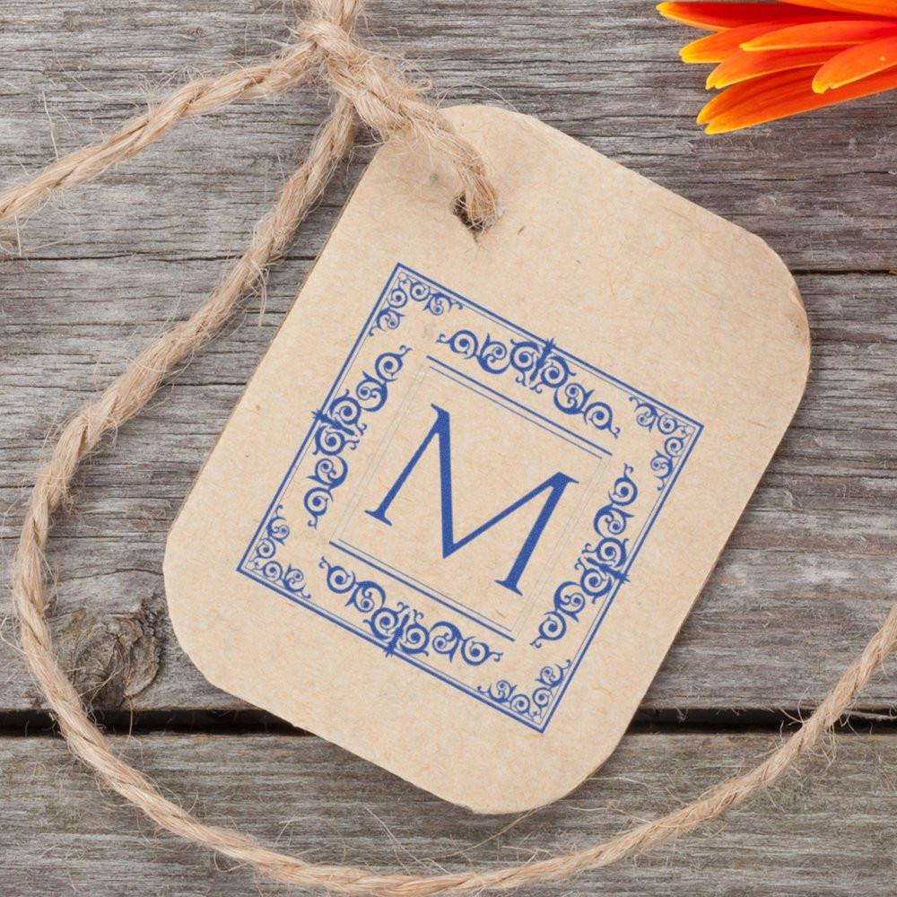 Custom monogram rubber stamp with blue letter M on kraft gift tag, ideal for personalized packaging and branding.