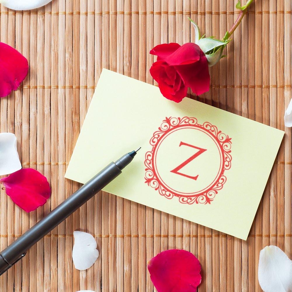 Custom monogram rubber stamp impression with letter Z on a card, styled with rose petals and a pen.