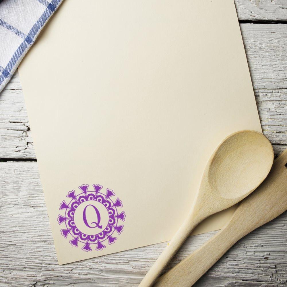 Cream monogram Q label for kitchen branding beside a wooden spoon on a rustic tabletop.