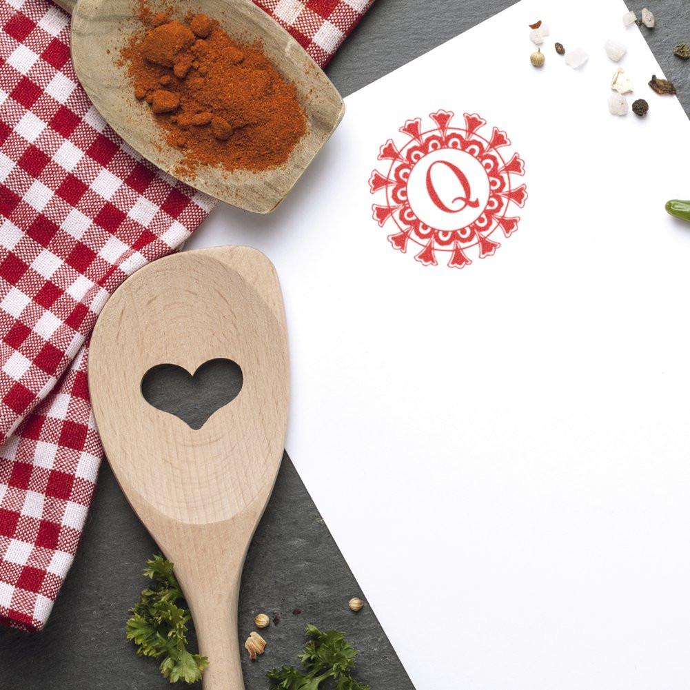 Spice seasoning flat lay with wooden spoon, herbs and checkered cloth beside red Q logo on white background.