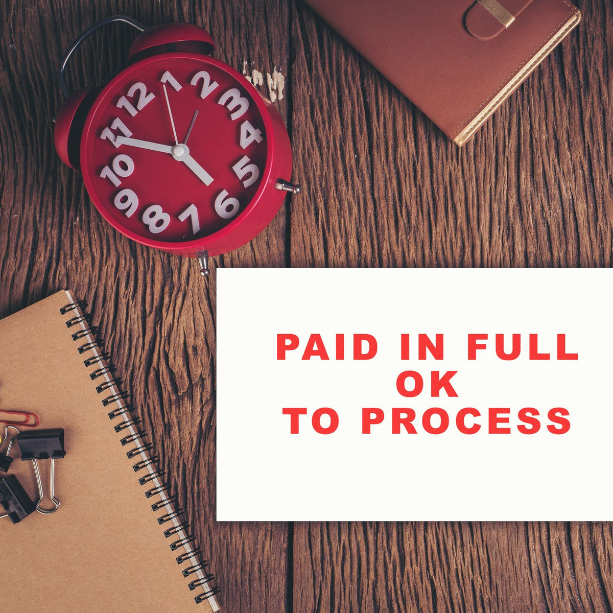 Alarm clock and paperwork on desk with PAID IN FULL OK TO PROCESS payment confirmation sign.