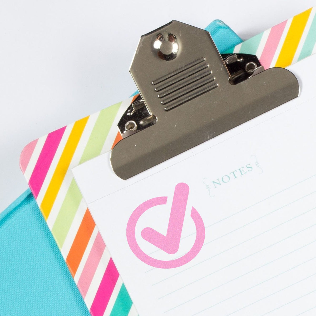 Magnetic clip on colorful striped notes page with checkmark symbol, illustrating checklist and reminder organization