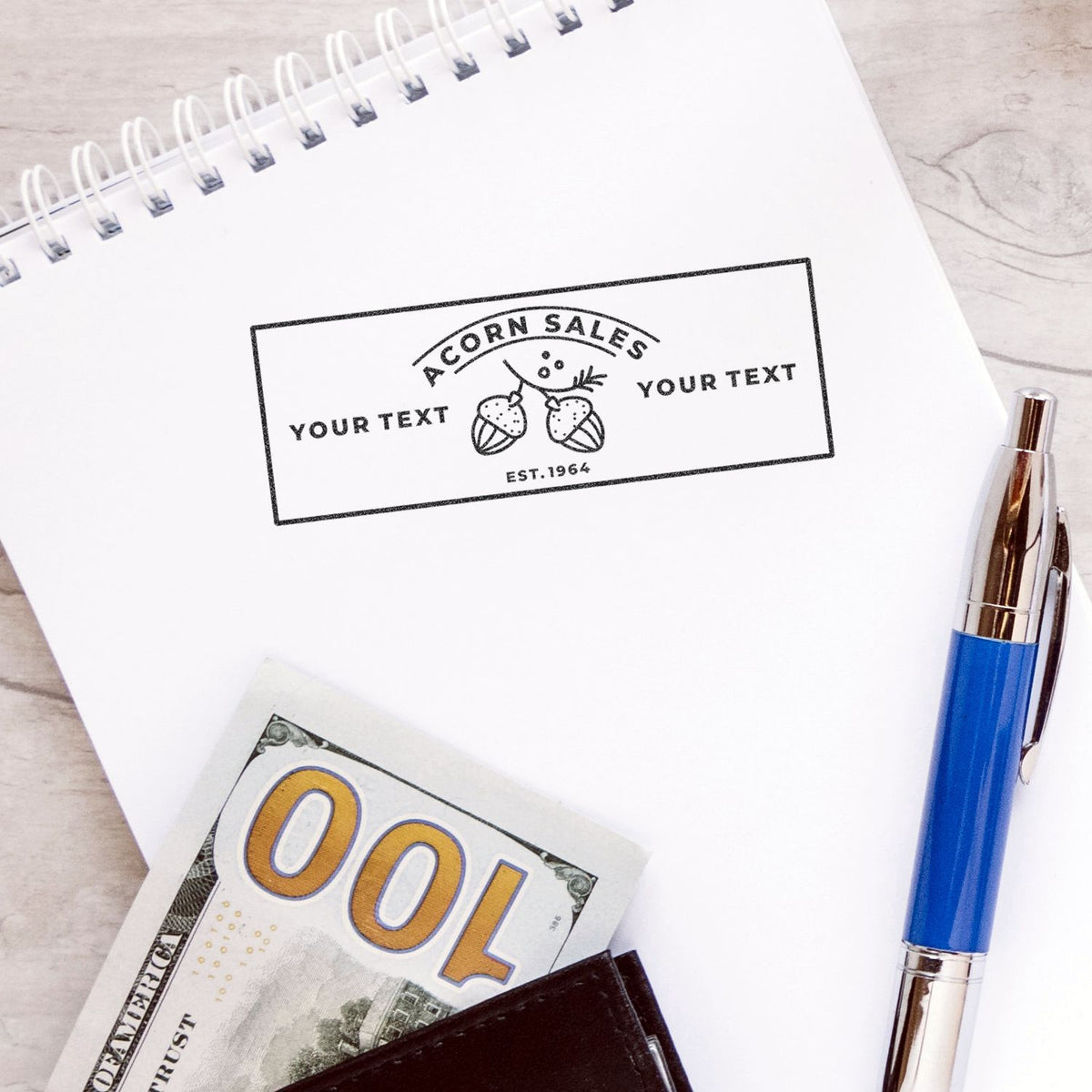 Close-up of Acorn Sales branded notebook with custom text area, plus pen and cash, for promotional business stationery marketing.