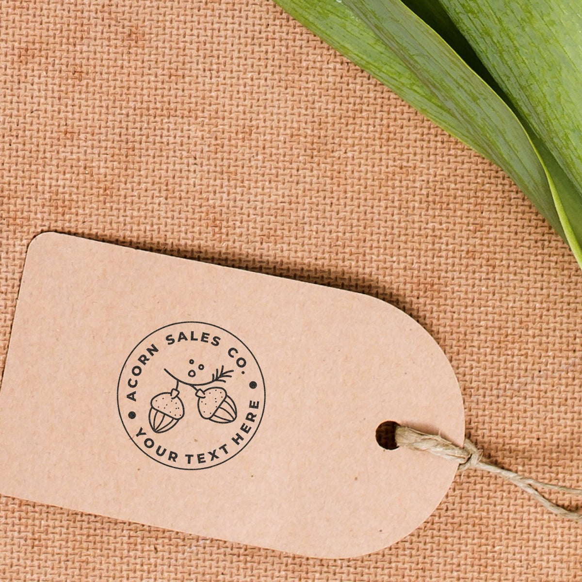 Acorn Sales kraft tag with acorn logo on gift box, tied with twine and near green leaves for seasonal branding