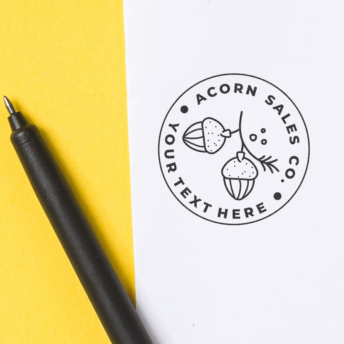 Acorn logo sticker stamp reading ACORN SALES HERE with acorn and candy icons on stationery beside a yellow pen.