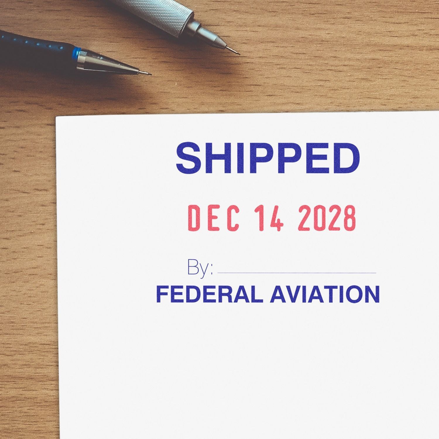 Shipping label stamp on paper with SHIPPED Dec 14 2028 and Federal Aviation text on a wooden desk with pens.