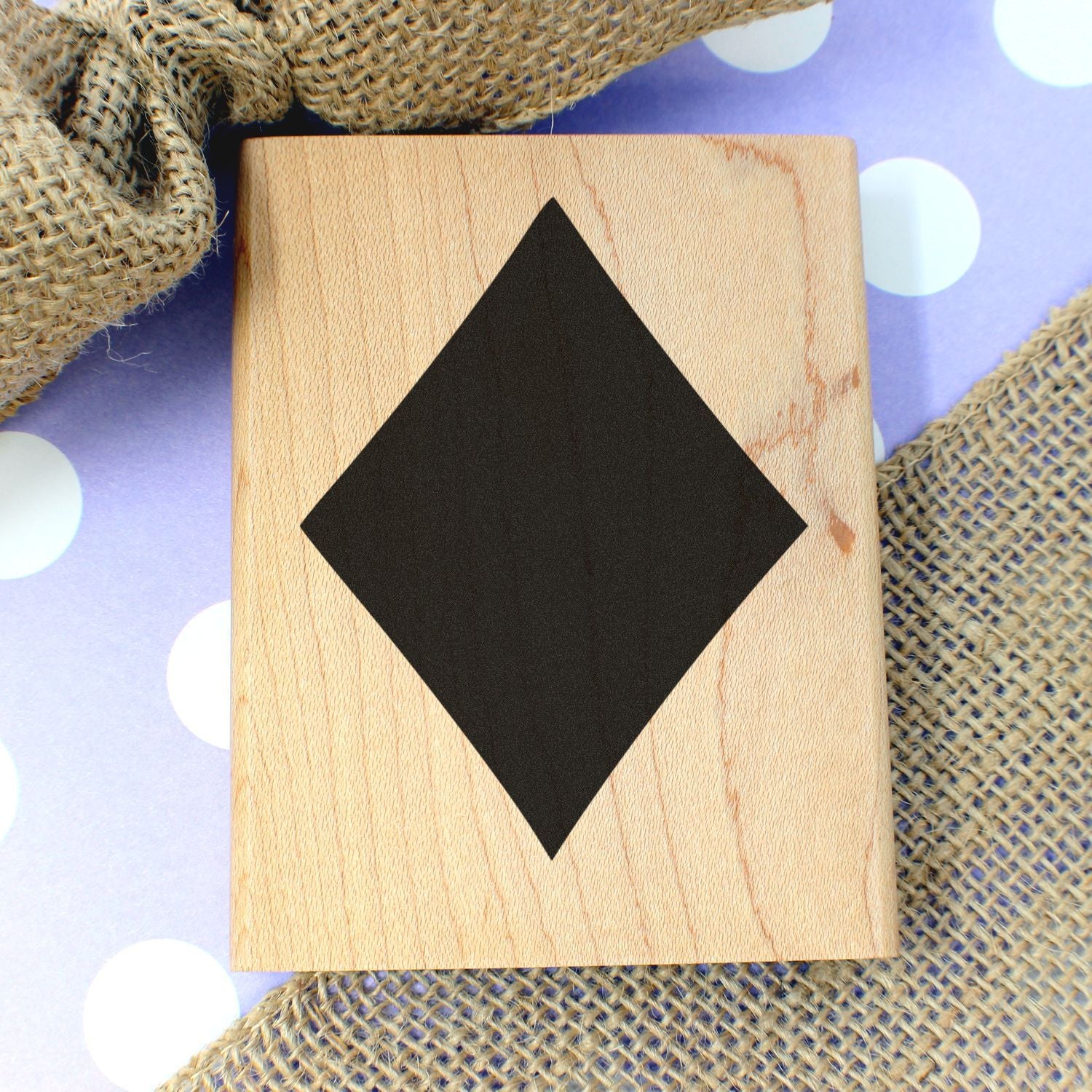 Wooden diamond-shaped stamp block on burlap and polka dot background, handmade craft design tool.