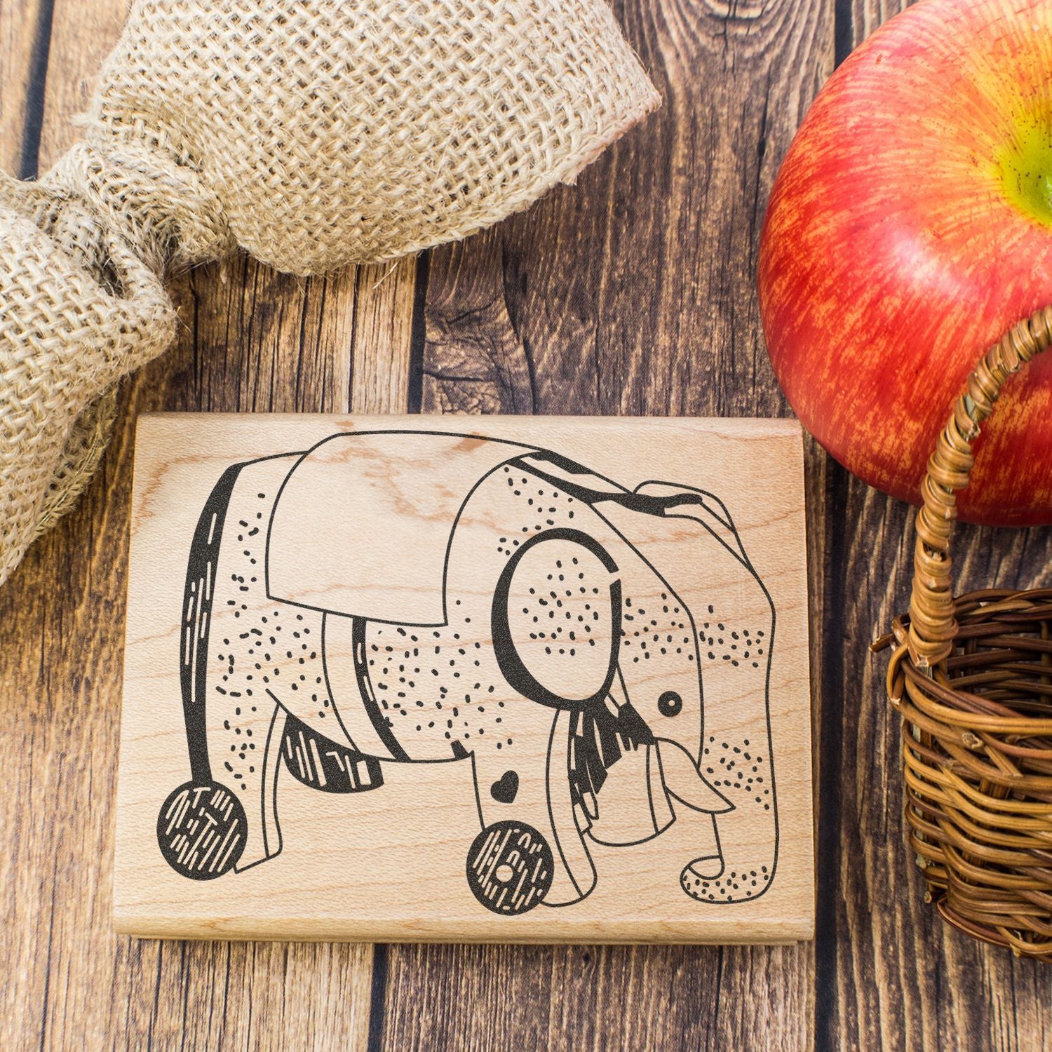 Wooden elephant stamp on rustic wood background with burlap and apple, farmhouse decor close-up.