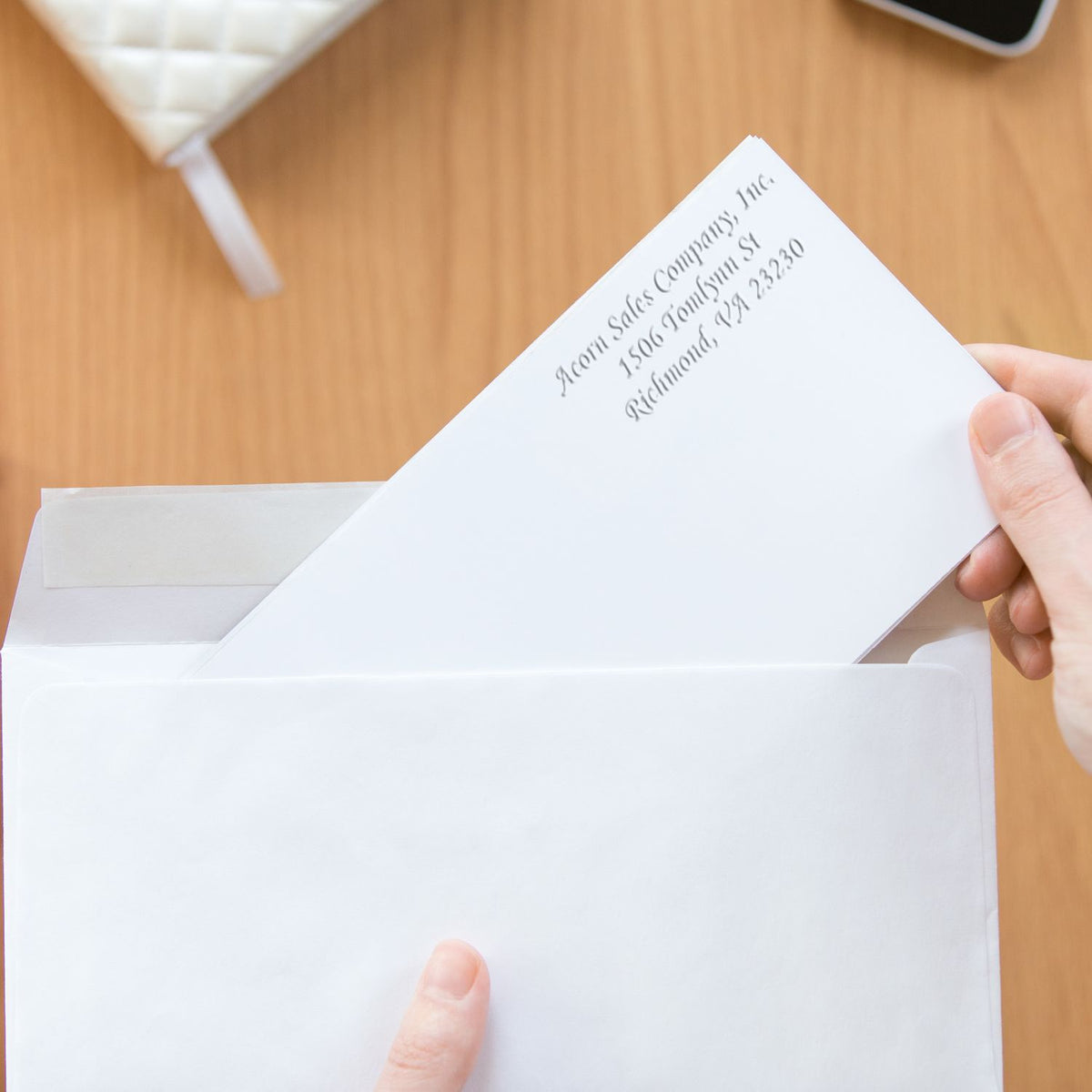 Hand placing a white business letter in an envelope on a wooden desk