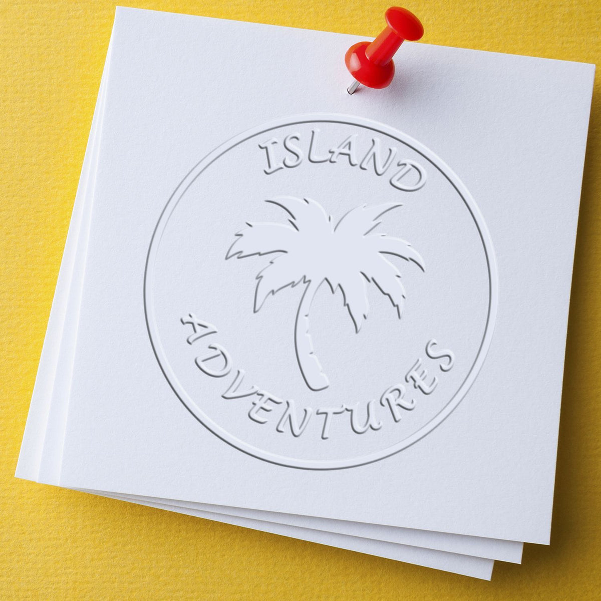 Embossed Island Adventures logo with palm tree on white paper pinned with a red pushpin on a yellow background.