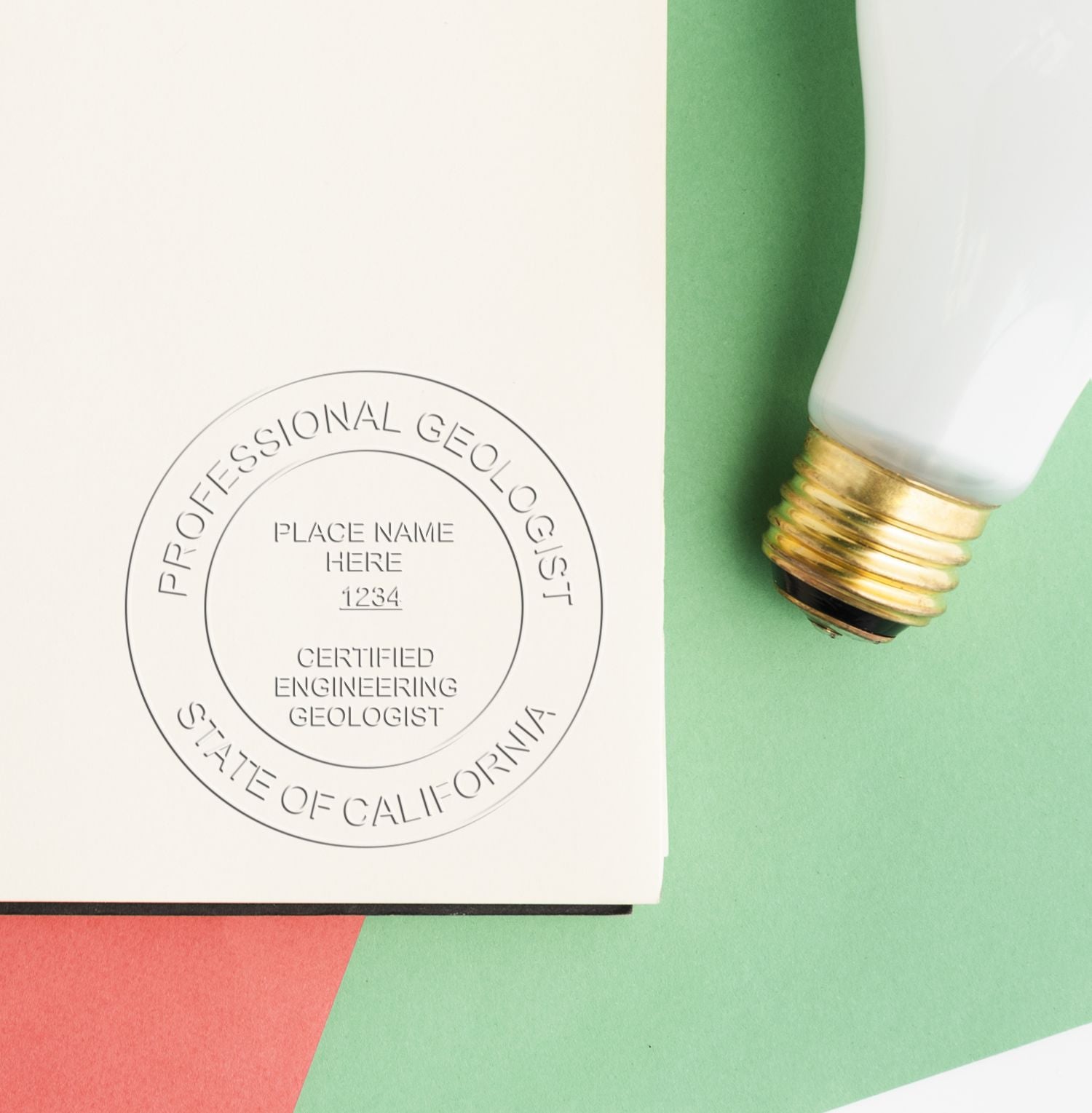 Professional geologist embossed seal stamp on paper next to a white and gold pen on a green background.