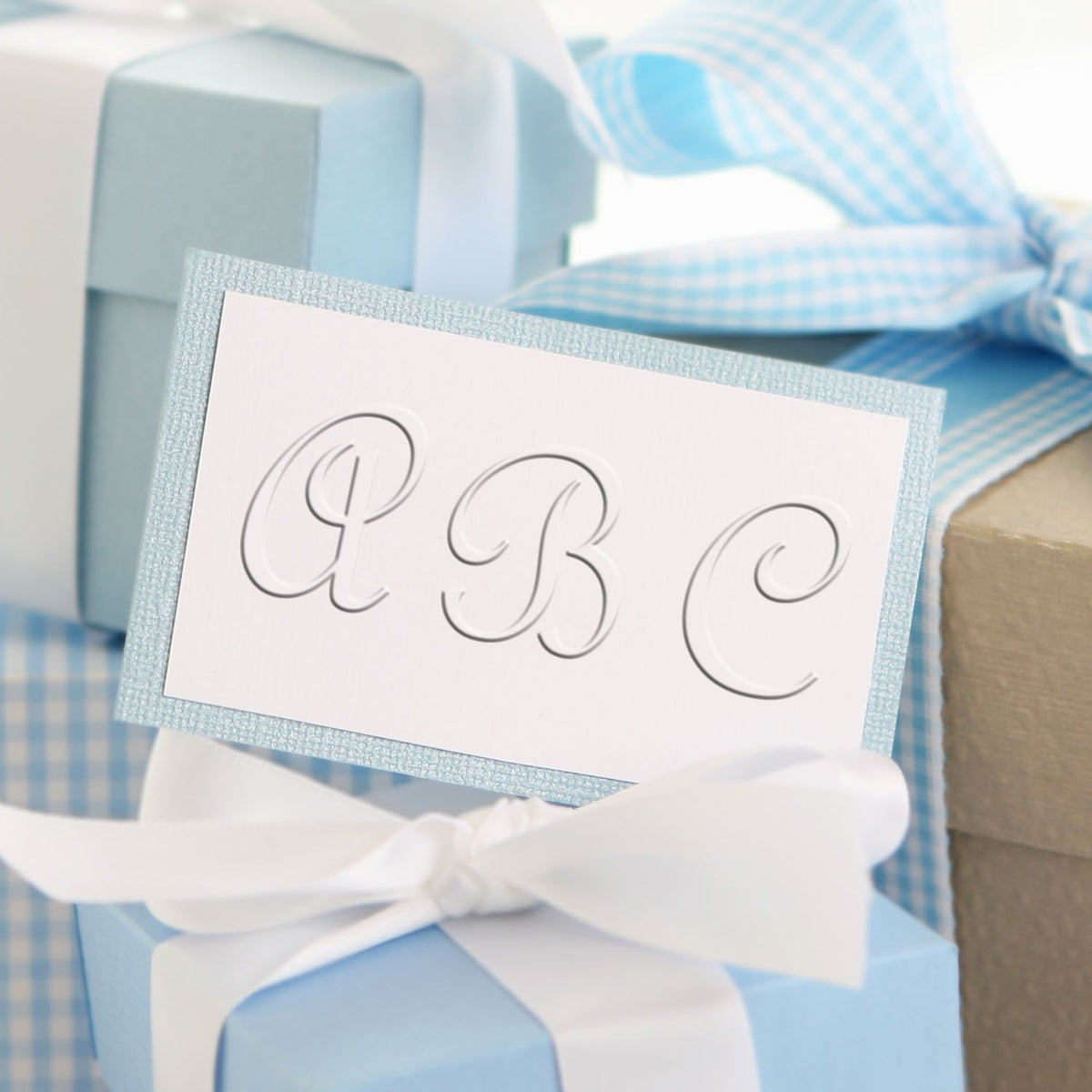 Elegant blue baby shower gift boxes with white ribbon and personalized ABC monogram card.