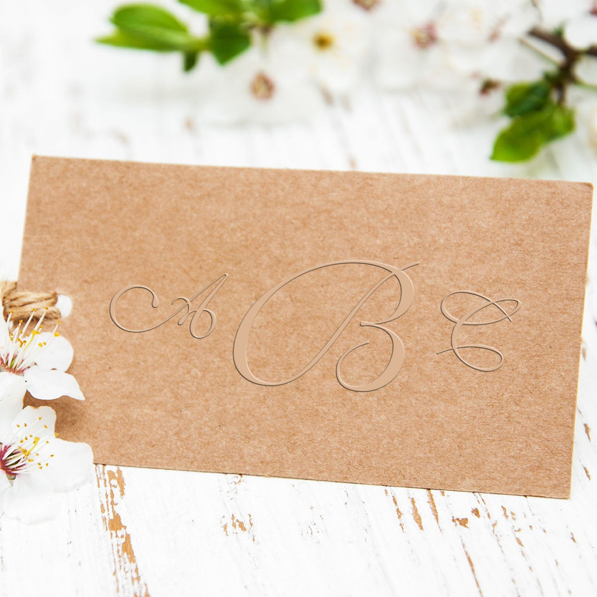 Elegant kraft paper card with decorative A B E lettering and spring blossoms on a white rustic background.