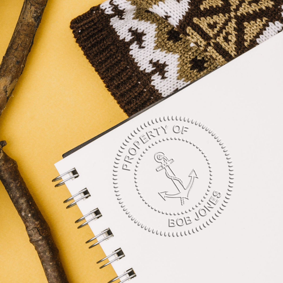 Custom spiral notebook with Property of Bob Jones anchor logo, knit fabric pattern, and rustic branches on a yellow background.