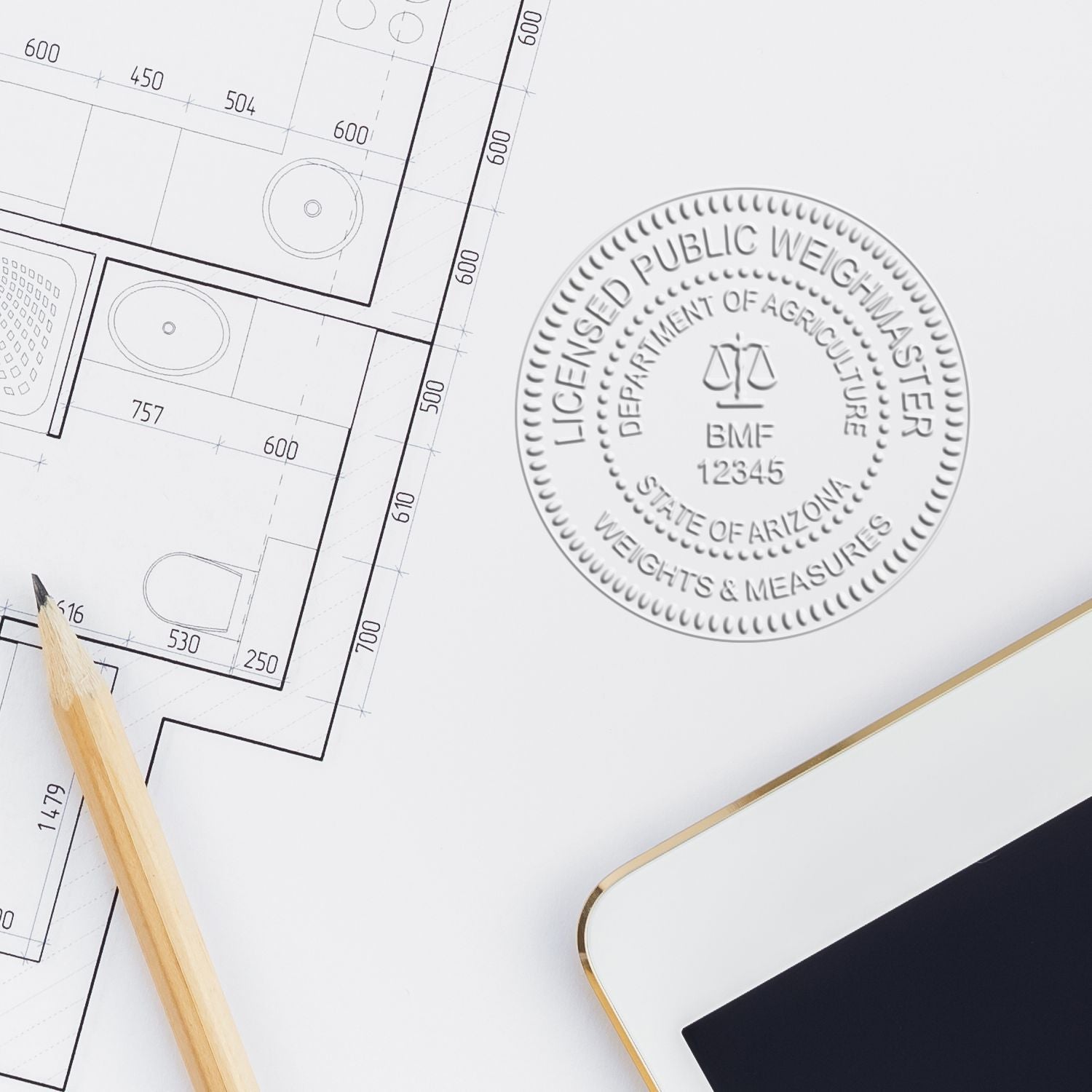 Architectural floor plan blueprint with licensed public weighmaster stamp, pencil, and tablet on desk, showing construction drawing and measurement details.