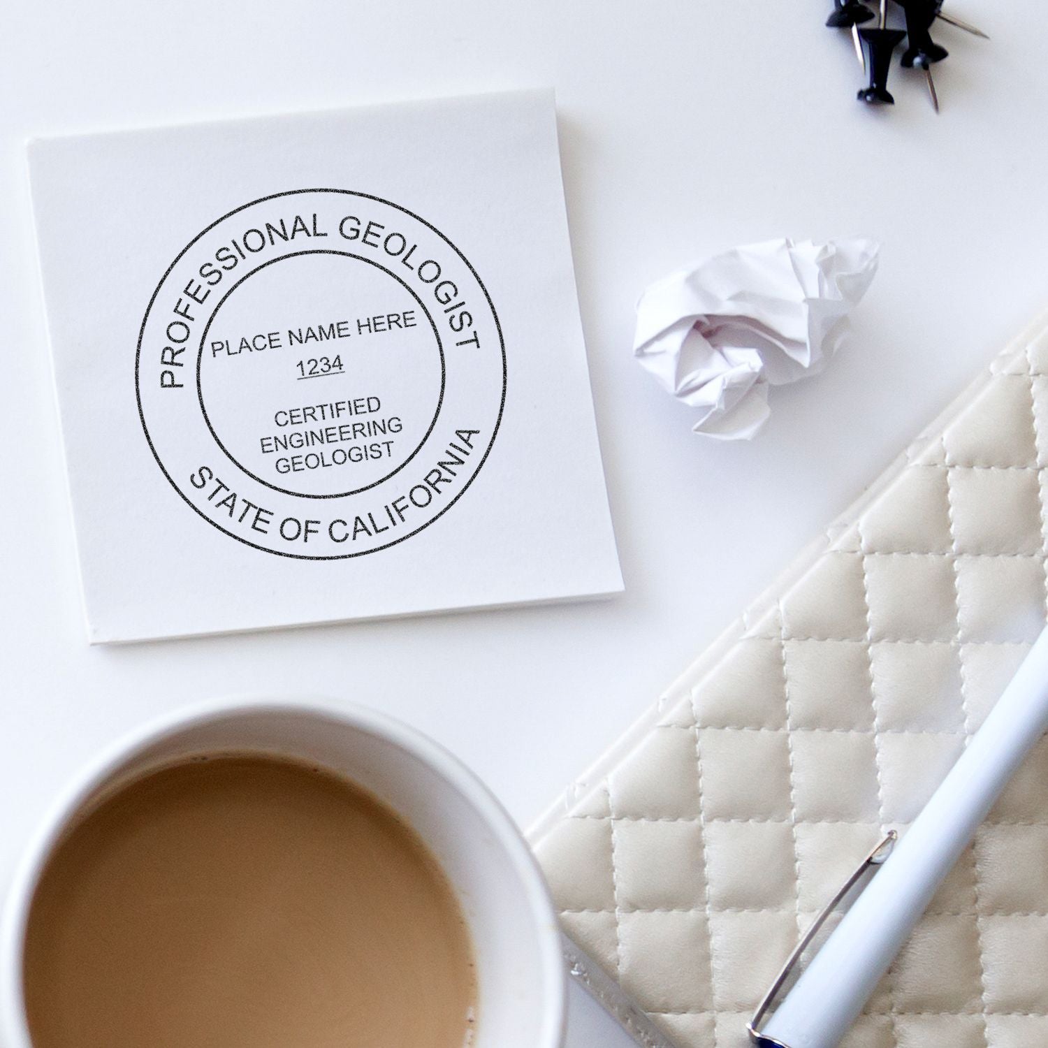 Professional geologist California certification stamp on white notebook with coffee cup, pen, and crumpled paper on desk.