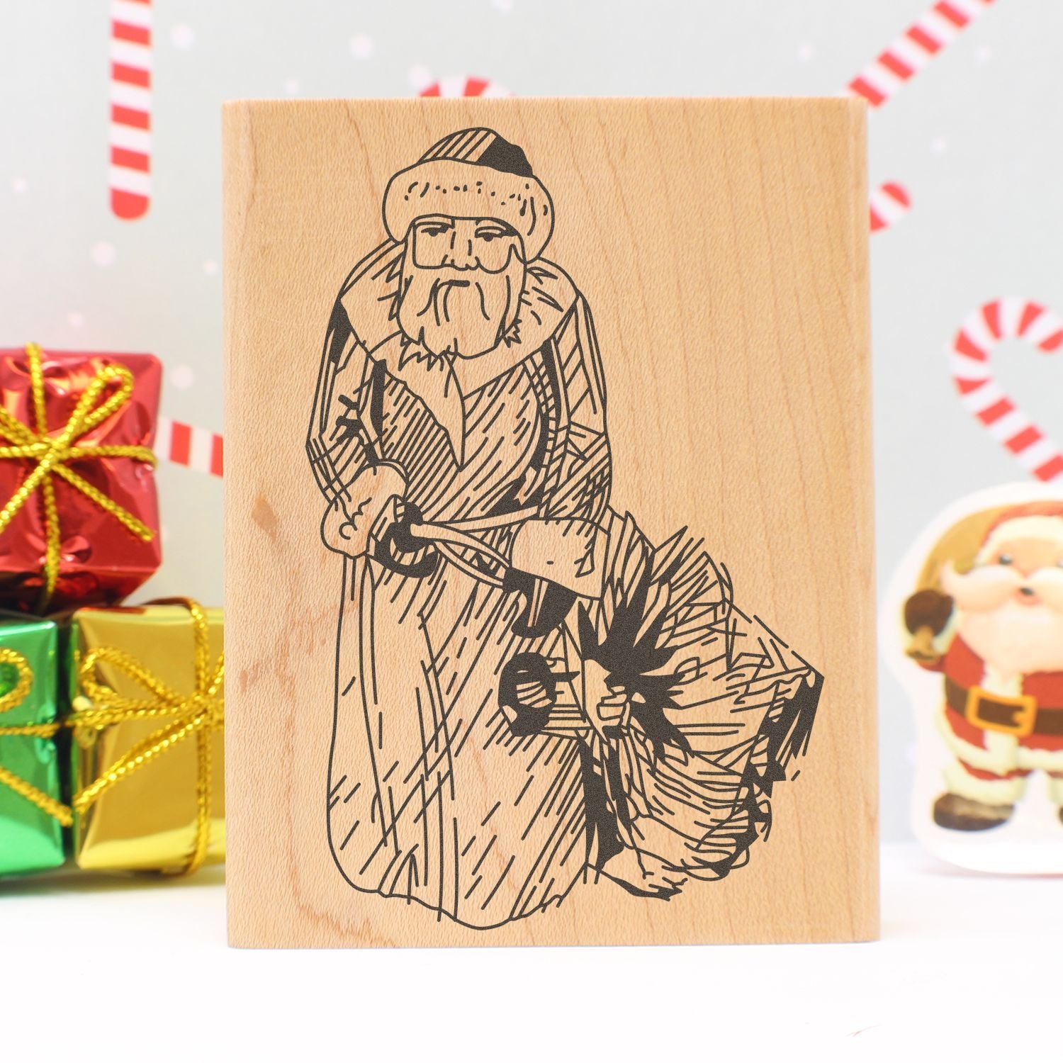 Wooden Christmas stamp with Santa Claus illustration, festive holiday gift packaging and candy cane background.