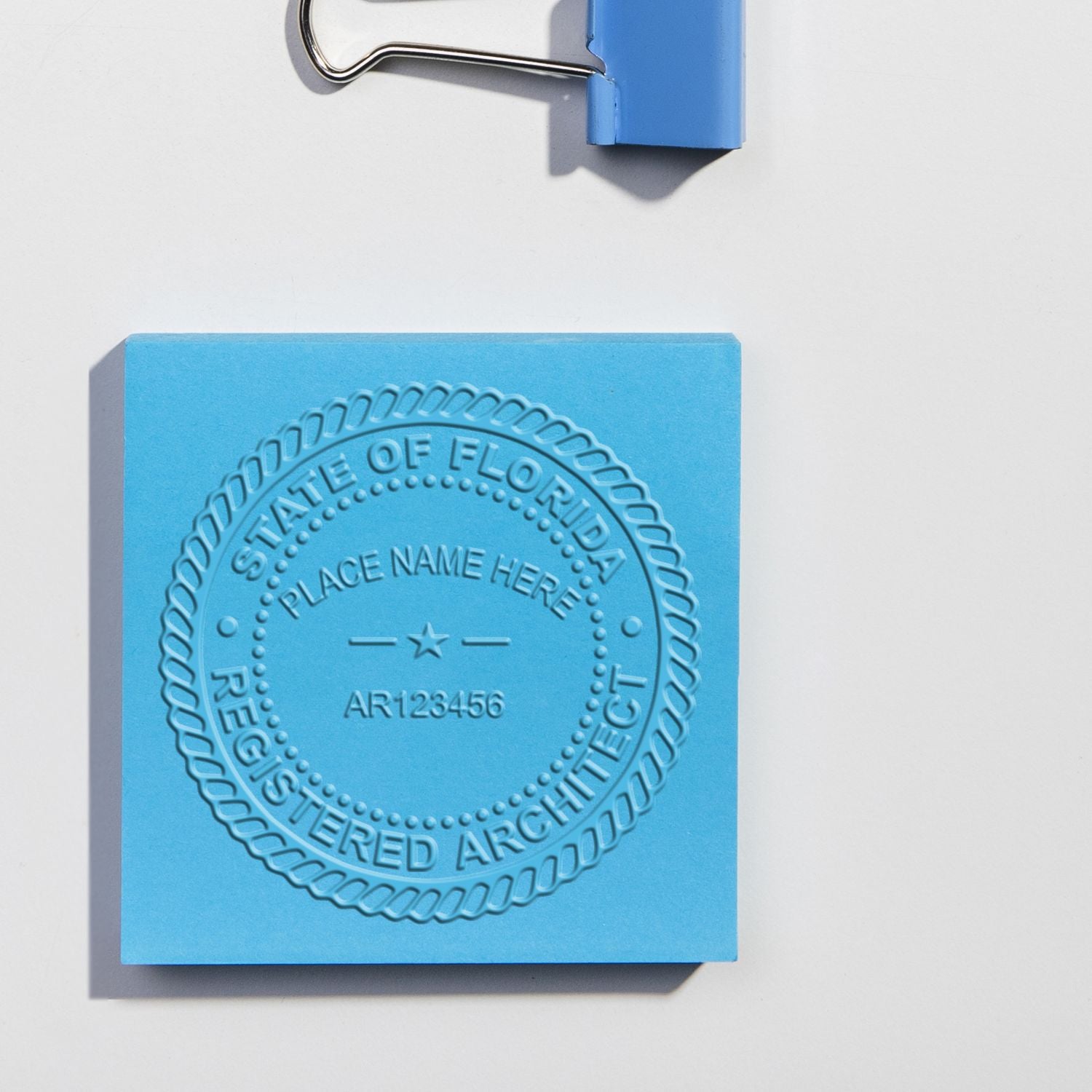 Blue embossed State of Florida registered architect seal clipped on white paper.