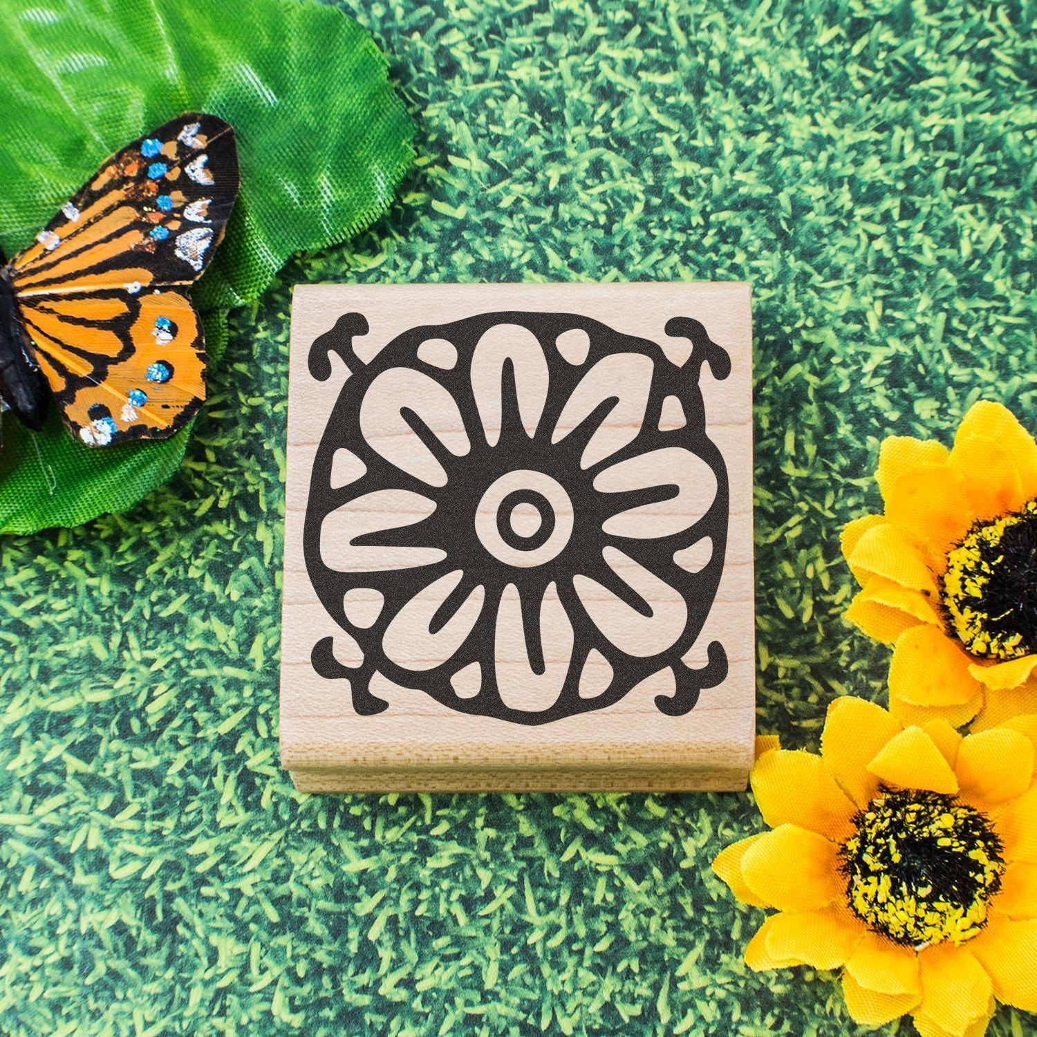 Wooden floral mandala stamp with butterfly wing and sunflowers on a green garden background