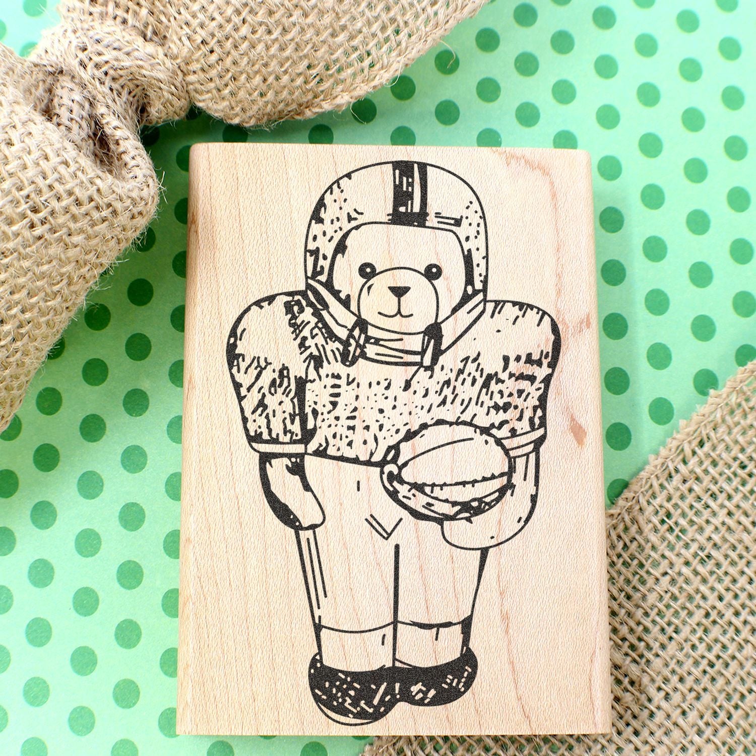 Wooden stamp with cute astronaut teddy bear design on green polka dot background with burlap fabric.