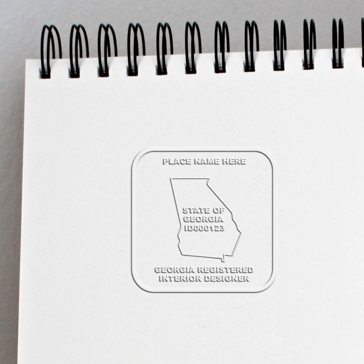 White spiral-bound notebook cover with embossed Georgia Registered Interior Designer seal and state of Georgia outline.
