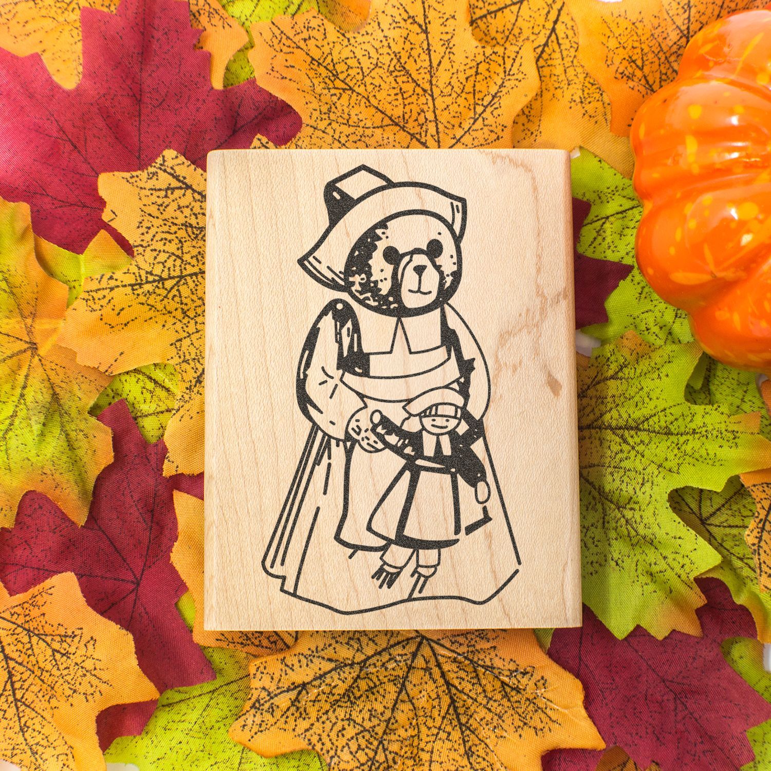 Autumn-themed wooden stamp with a cute bear illustration on colorful fall leaves and a pumpkin background.